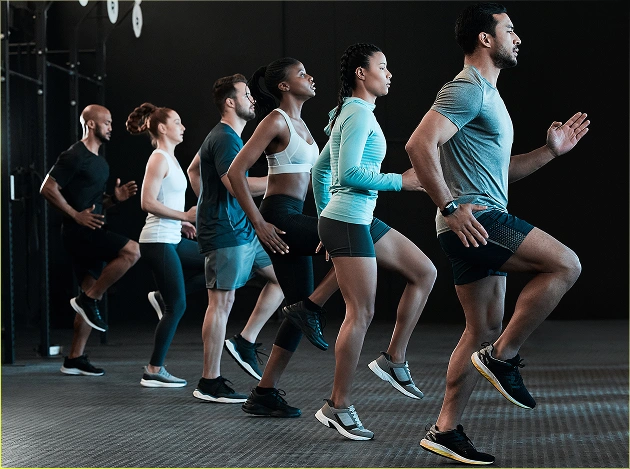 Een groep mensen doet tijdens de training in de fitnessruimte een oefening waarbij ze hun knieën hoog optillen