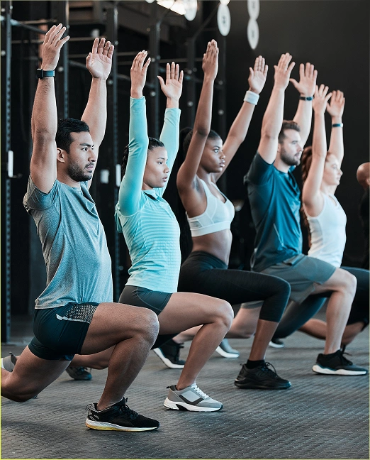 Een groep mensen doet lunges met opgeheven armen in de fitnessruimte