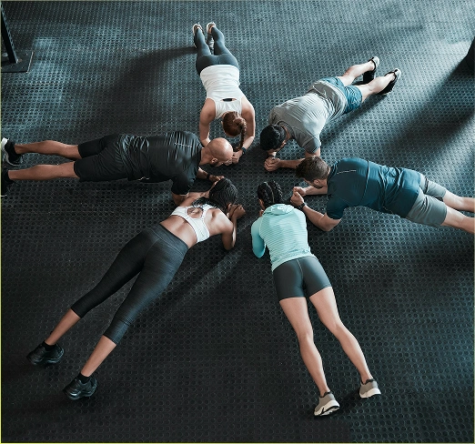 Een groep mensen doet de plank-oefening terwijl ze in een kring op de vloer liggen